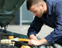 Photo of a young male mechanic examining under the hood of a car